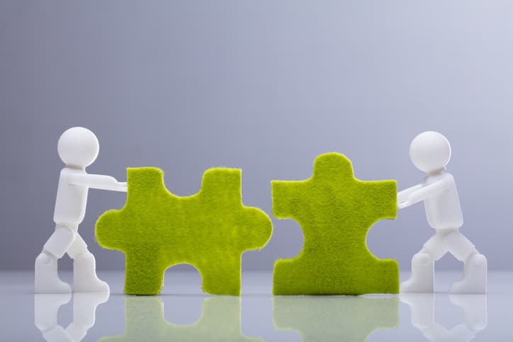 Two figures push two large, green puzzle pieces together