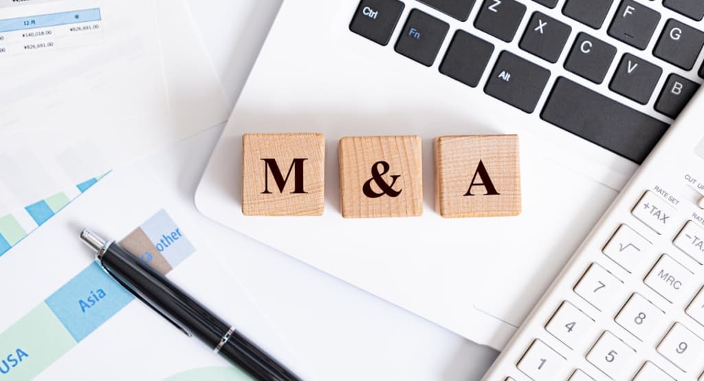 Wooden blocks with the characters 'M&A' spelled out on top of an open laptop