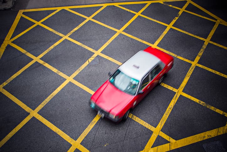 Image of a red Hong Kong taxi driving across yellow road markings