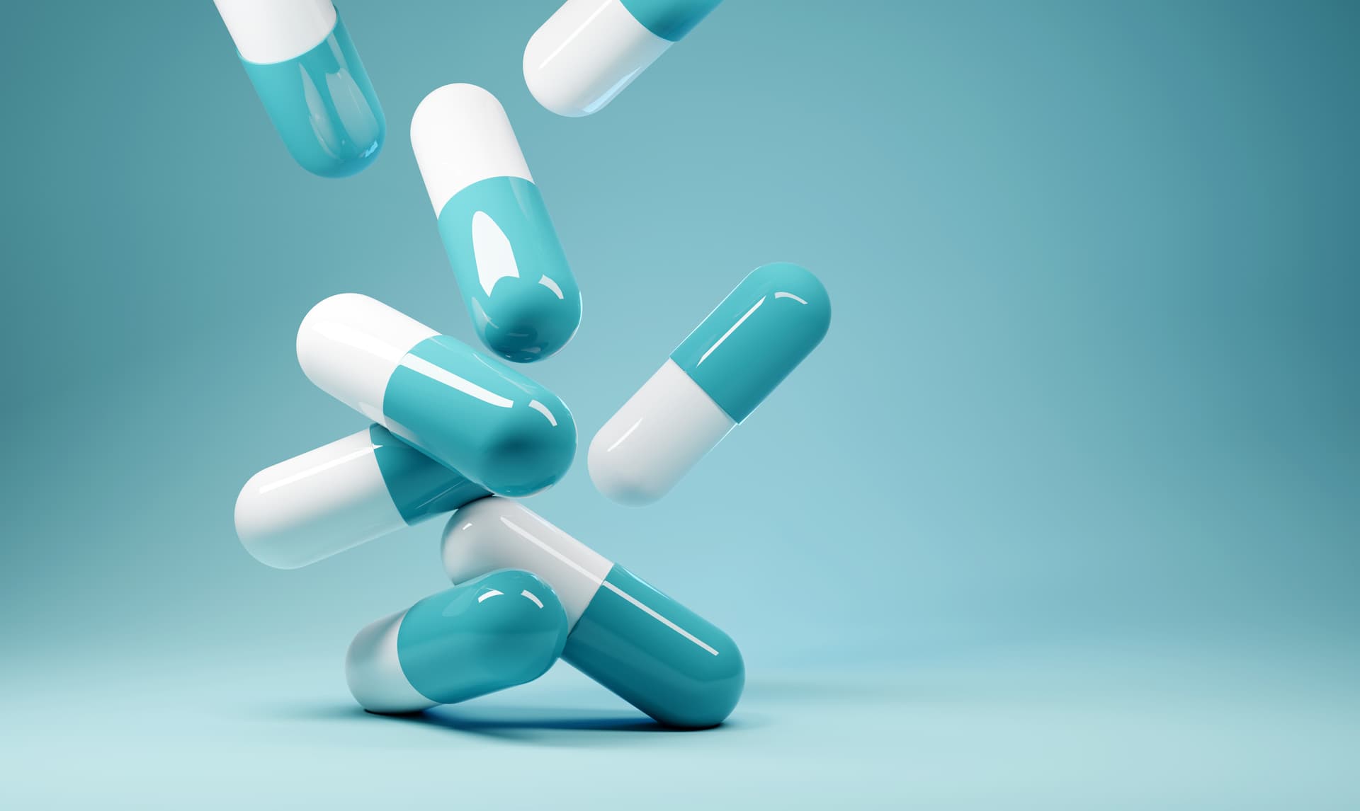 Cyan and white medicinal capsules falling onto a turquoise background