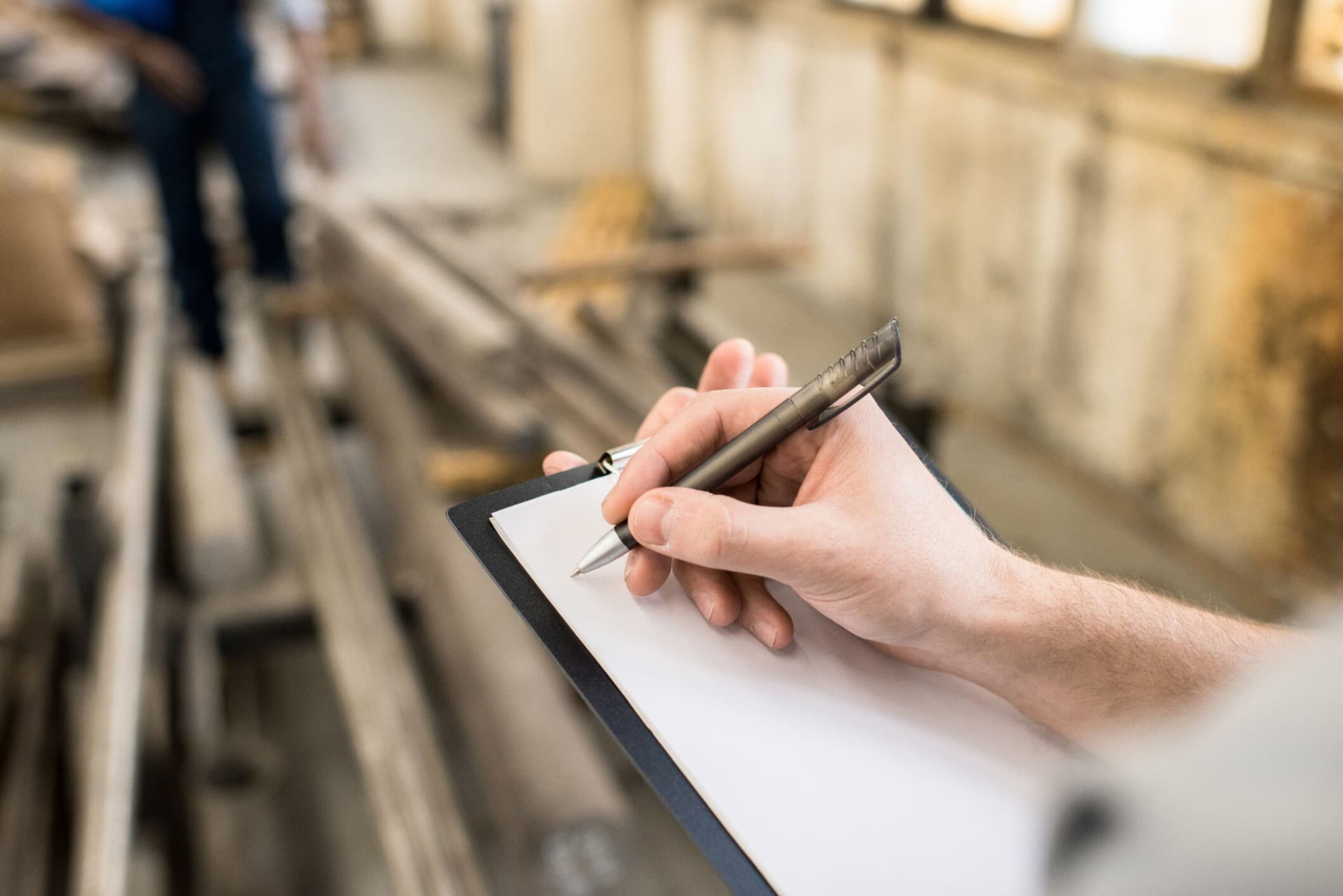 Close-up of unrecognizable quality control specialist holding clipboard with blank paper and writing information about production at plant
