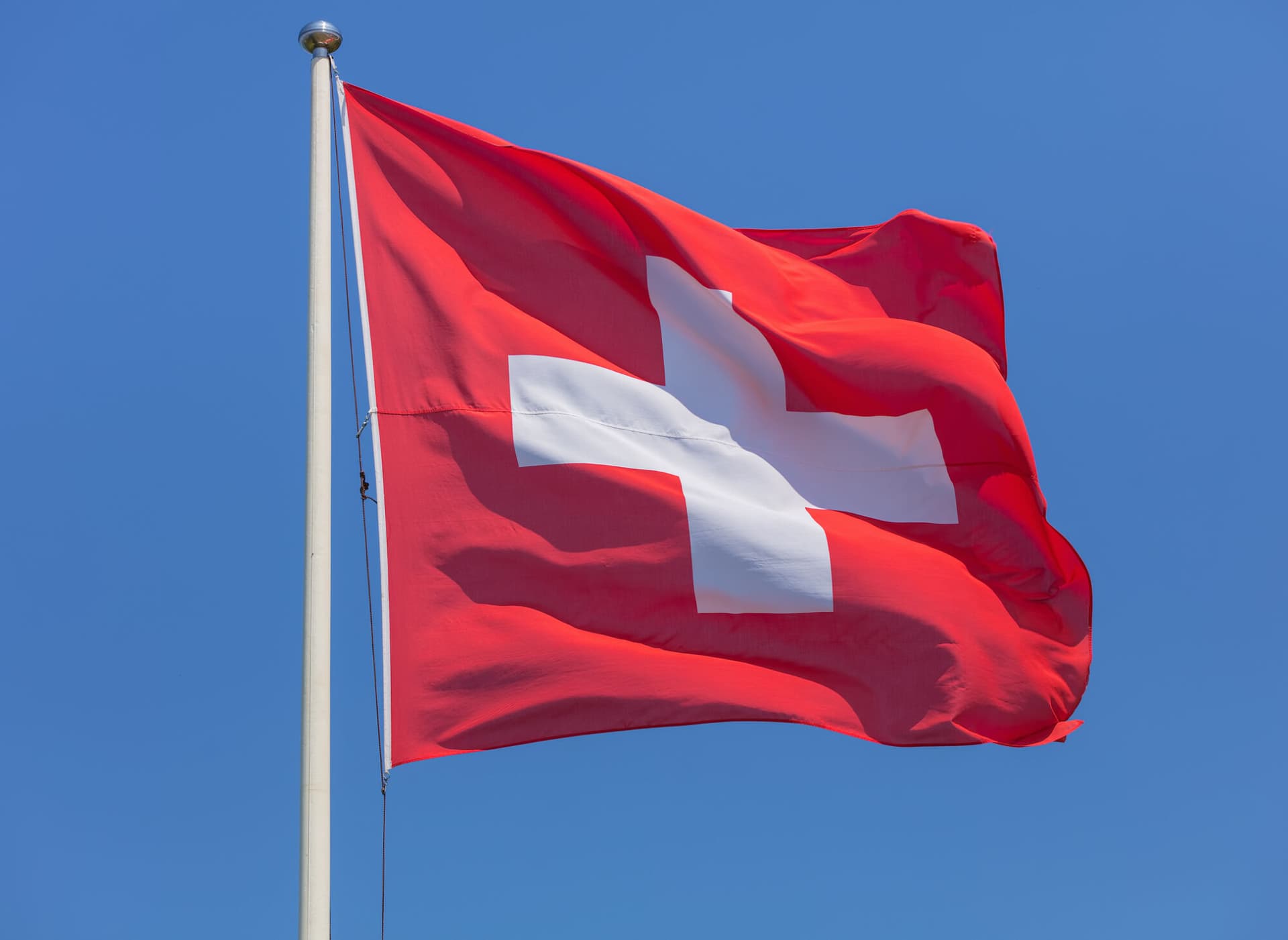 https://www.gettyimages.co.uk/detail/photo/flag-of-switzerland-against-clear-blue-sky-on-a-royalty-free-image/1031668640?phrase=swiss+flag