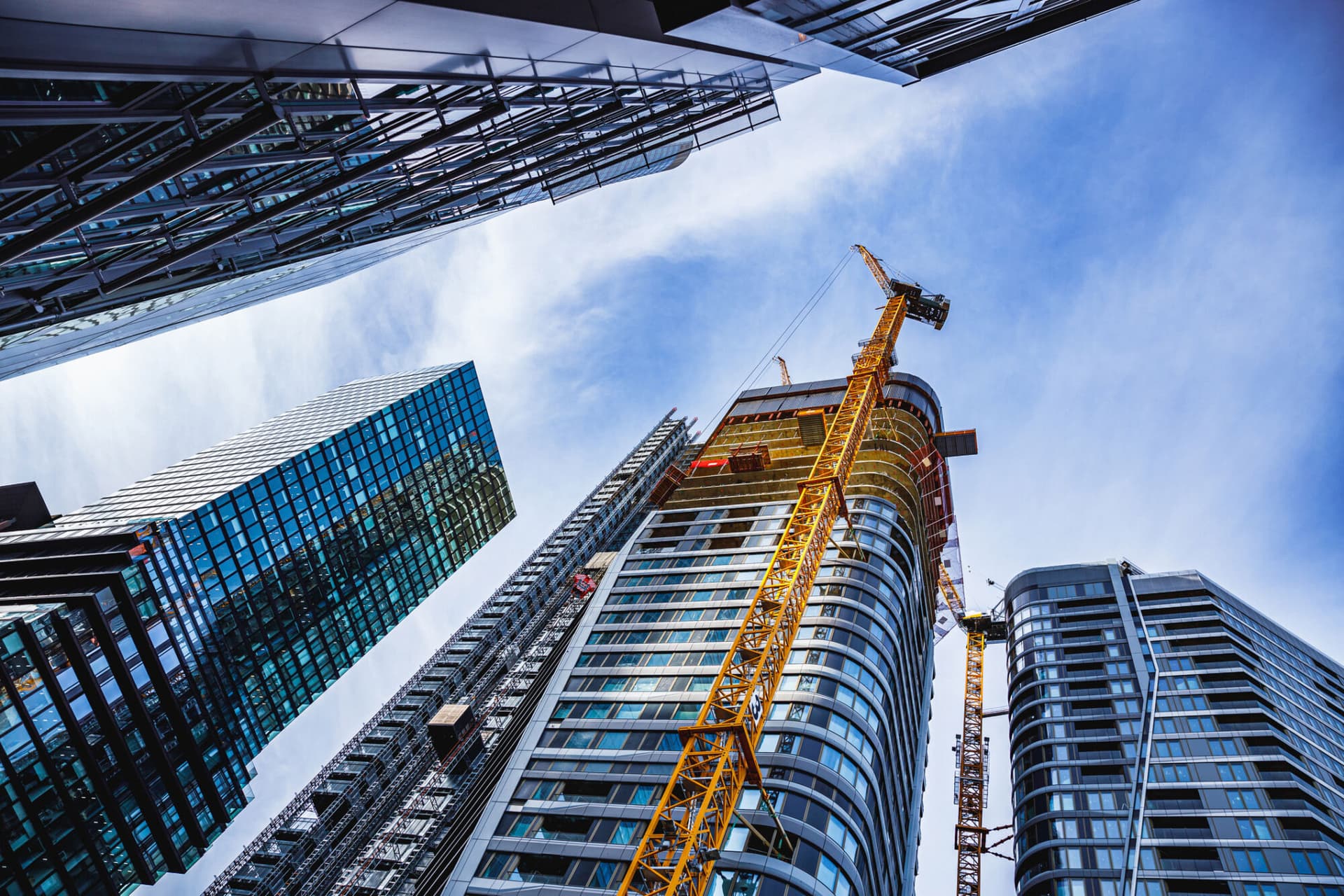 Low angle view of concrete and steel skyscrapers in blue glass with cranes around